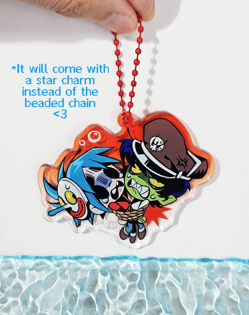 Puede incluir: Un dije de acr&iacute;lico con una ilustraci&oacute;n de dibujos animados de un personaje de pelo azul con m&aacute;scara blanca y un personaje de piel verde con sombrero marr&oacute;n, atados con una cuerda. El texto dice: *It will come with a star charm instead of the beaded chain <3.