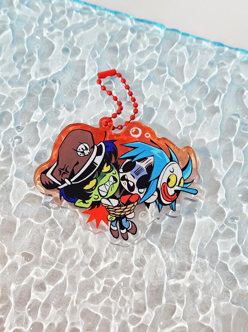 Puede incluir: Un llavero de acr&iacute;lico transparente con una ilustraci&oacute;n de dibujos animados de un personaje de piel verde con sombrero de pirata marr&oacute;n que sostiene a un personaje de pelo azul atado con una cuerda y una m&aacute;scara blanca de nariz larga.