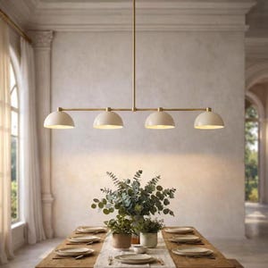 Puede incluir: Una lámpara de araña moderna de cuatro luces con acabado de latón y pantallas de cúpula blanquecinas cuelga sobre una mesa de comedor de madera. La mesa está puesta con platos, cubiertos y un centro de mesa de vegetación. La lámpara mide aproximadamente 122 cm de largo.