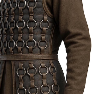 May include: A dark brown tunic featuring a chest and waist panel reinforced with a grid of dark leather straps and interconnected metal rings. The garment has long, solid brown sleeves and a structured, layered design with a defined horizontal waistband.