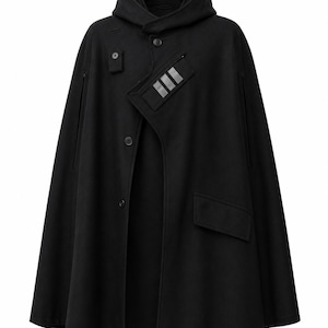 May include: A black hooded cape featuring a front button closure, a small rectangular chest pocket with three silver-toned reflective stripes, and a larger flap pocket on the lower left side. The garment has a structured hood and arm slits.