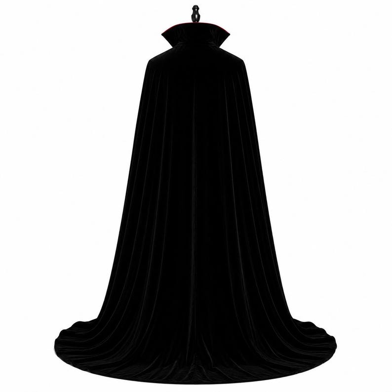 May include: A floor-length black velvet cape featuring a high, stiffened stand-up collar with a deep red inner lining. The garment is displayed on a mannequin, showcasing a full, flowing silhouette that drapes down to the floor in vertical folds.