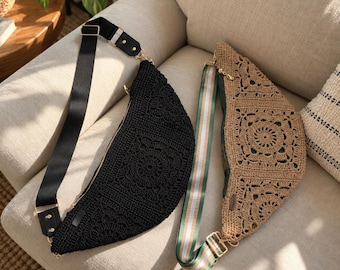 May include: Two crescent-shaped crossbody bags featuring intricate crochet patterns. One bag is solid black with a plain black strap, while the other is tan with a green, white, and gold striped strap. Both bags have gold-tone hardware.