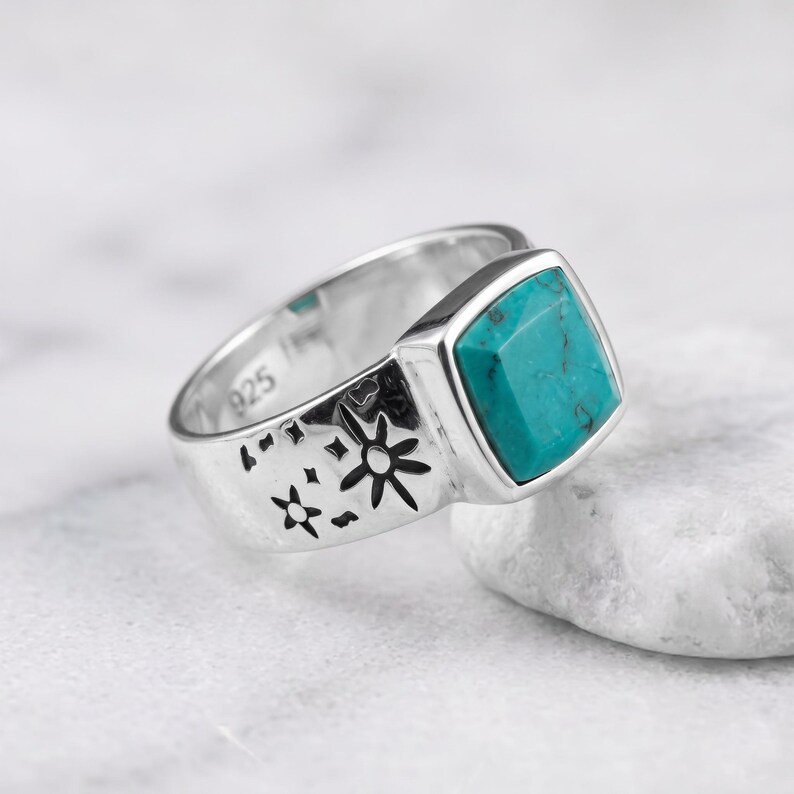 Peut inclure: Une bague en argent sterling orn&eacute;e d'une pierre turquoise de taille carr&eacute;e et de motifs d'&eacute;toiles grav&eacute;s sur l'anneau. L'int&eacute;rieur de l'anneau porte clairement le poin&ccedil;on 925, indiquant la teneur en argent de ce bijou en m&eacute;tal poli.
