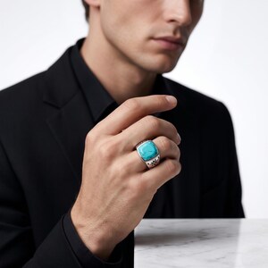 Peut inclure: Une bague en argent orn&eacute;e d'une grande pierre turquoise de forme carr&eacute;e aux bords arrondis. L'anneau est fabriqu&eacute; en argent poli et pr&eacute;sente un motif floral ou en &eacute;toile finement grav&eacute; en noir sur les c&ocirc;t&eacute;s de la monture.