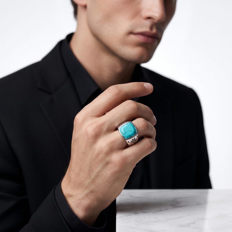 Peut inclure: Une bague en argent orn&eacute;e d'une grande pierre turquoise de forme carr&eacute;e aux bords arrondis. L'anneau est fabriqu&eacute; en argent poli et pr&eacute;sente un motif floral ou en &eacute;toile finement grav&eacute; en noir sur les c&ocirc;t&eacute;s de la monture.