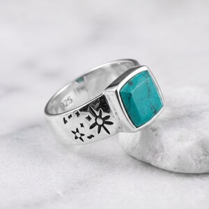 Peut inclure: Une bague en argent sterling orn&eacute;e d'une pierre turquoise de taille carr&eacute;e et de motifs d'&eacute;toiles grav&eacute;s sur l'anneau. L'int&eacute;rieur de l'anneau porte clairement le poin&ccedil;on 925, indiquant la teneur en argent de ce bijou en m&eacute;tal poli.