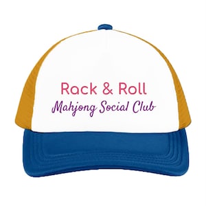 May include: A trucker hat with a white front panel, gold mesh back panels, and a blue brim. The front features the text "Rack & Roll" in pink and "Mahjong Social Club" in purple. The hat has a small blue button on the top center.