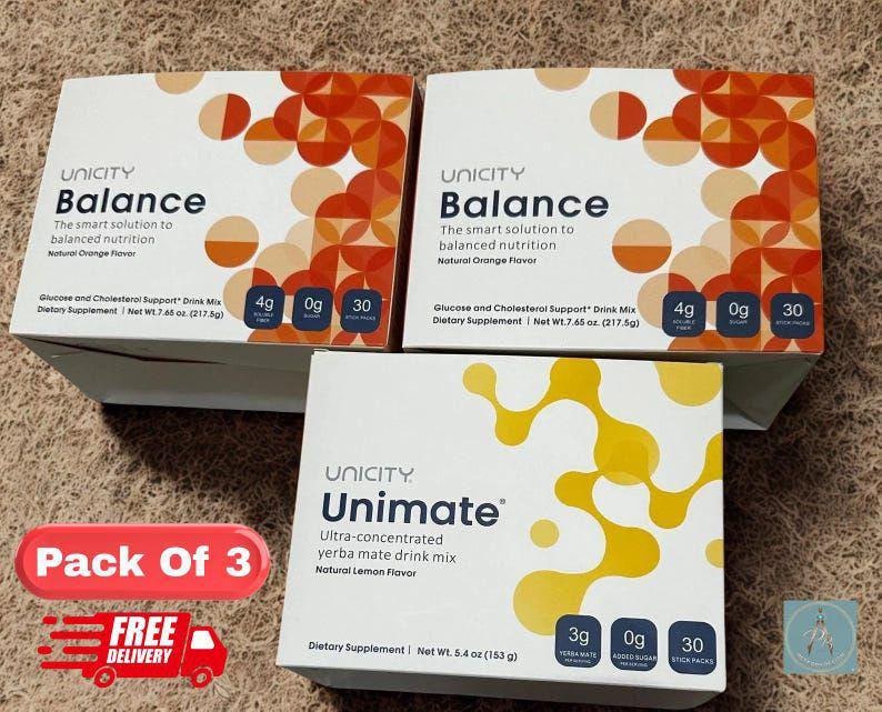 Op de afbeelding: Twee witte dozen Unicity Balance drankmix met oranje geometrische patronen en &eacute;&eacute;n witte doos Unimate yerba mate drankmix met gele abstracte vormen, elk met 30 sticks voor eenmalig gebruik.