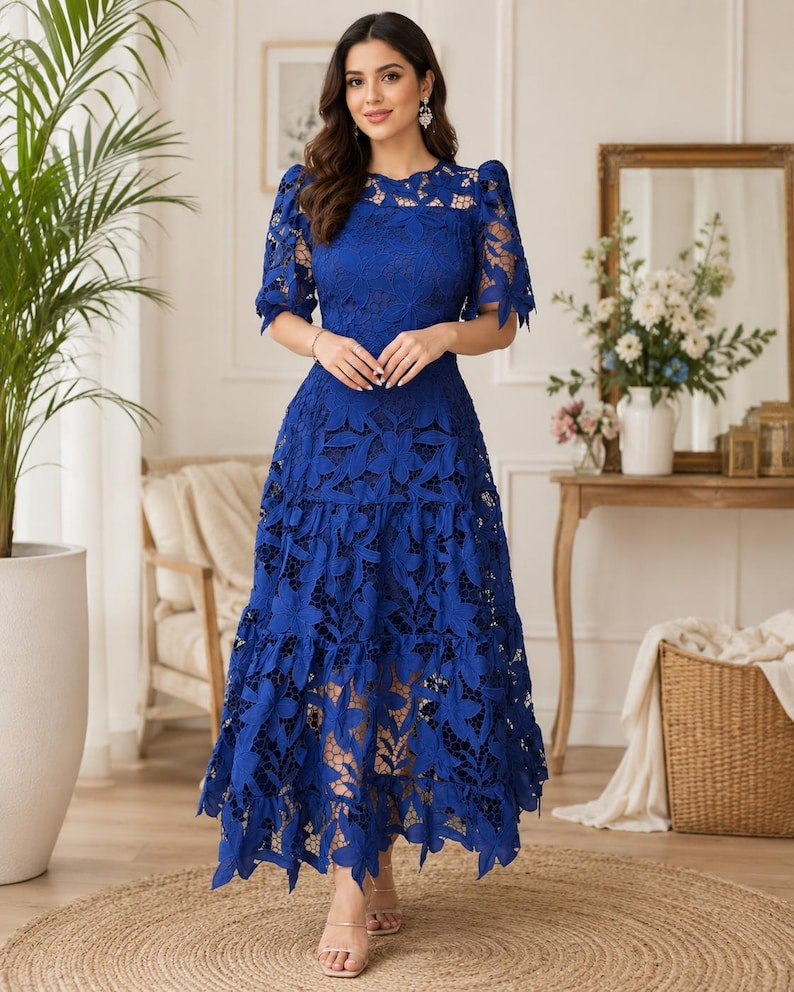 May include: A royal blue midi dress featuring intricate floral lace detailing throughout. The garment has short puff sleeves, a round neckline, and a tiered skirt design with a scalloped hemline. The lace pattern is dense and covers the entire dress.