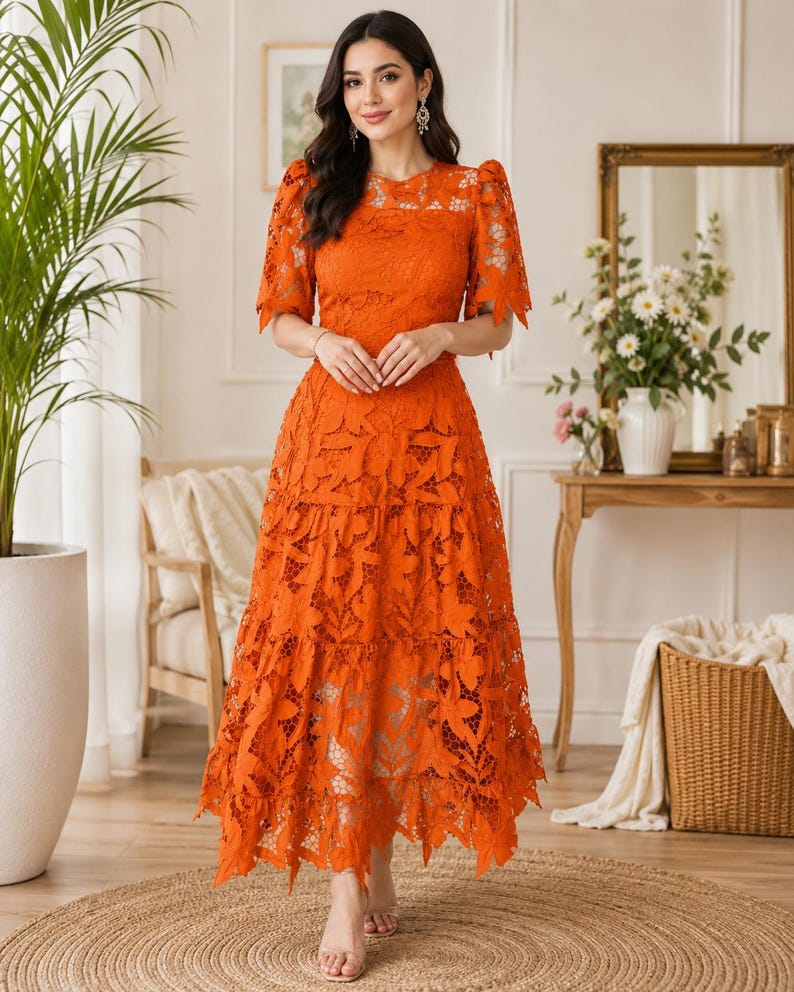 May include: A vibrant orange midi dress featuring intricate floral lace detailing throughout. The garment has short puff sleeves with tie accents, a round neckline, and a tiered skirt that falls to a mid-calf length with a scalloped hemline.