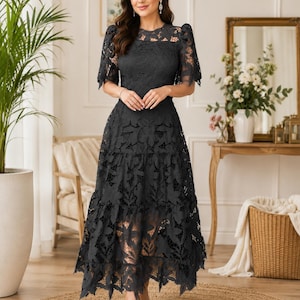 May include: A charcoal gray midi dress featuring intricate floral lace detailing, short puff sleeves, a round neckline, and a tiered skirt with a scalloped hemline. The garment is constructed with a solid lining underneath the lace overlay.