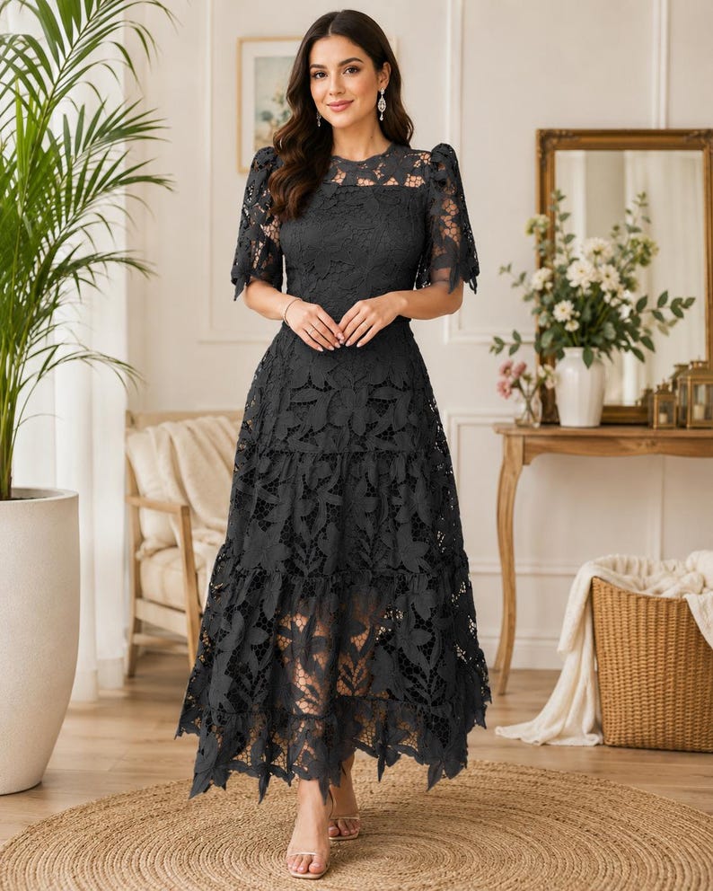 May include: A charcoal gray midi dress featuring intricate floral lace detailing, short puff sleeves, a round neckline, and a tiered skirt with a scalloped hemline. The garment is constructed with a solid lining underneath the lace overlay.