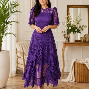 May include: A vibrant purple midi dress featuring intricate floral lace detailing throughout. The garment has short puff sleeves, a round neckline, and a tiered skirt with a scalloped hemline. The lace pattern is dense and covers the entire dress.