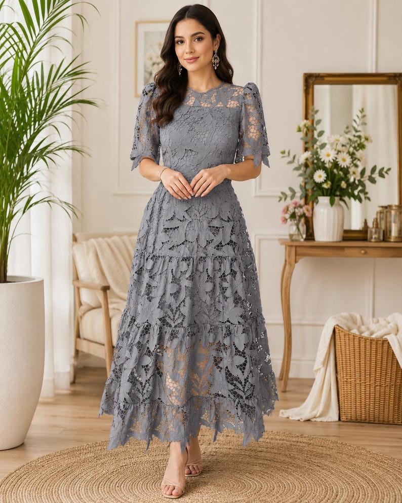 May include: A slate gray midi dress featuring intricate floral lace overlay, short puff sleeves, a round neckline, and a tiered skirt. The garment is constructed with a solid lining underneath the lace, creating a layered texture throughout the bodice and skirt.