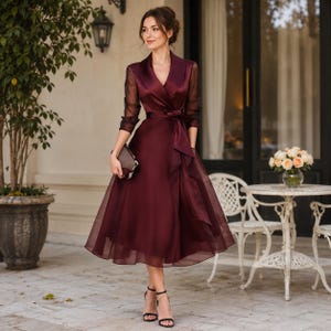 Può includere: Un abito midi color bordeaux scuro con corpetto a portafoglio, collo a scialle, maniche lunghe trasparenti e cintura in vita. La gonna presenta una silhouette ampia e svasata con orlo a strati. Abbinato a sandali neri con cinturini e tacco.