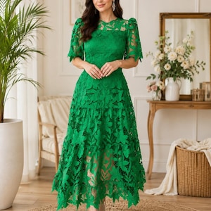 May include: A vibrant green midi dress featuring intricate floral lace detailing, short puff sleeves, a round neckline, and a tiered skirt with a scalloped hemline. The garment is constructed with a solid lining underneath the lace overlay.