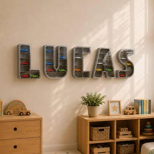 May include: A set of five wall-mounted display shelves shaped like the letters L, U, C, A, and S. Each letter-shaped shelf is constructed from grey material with clear front panels and contains multiple small toy cars on internal horizontal tiers.