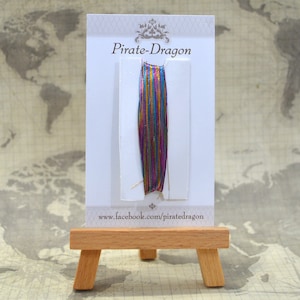 May include: A card with the text "Pirate-Dragon" and a sample of iridescent, multi-coloured metallic thread. The card is on a small wooden easel.