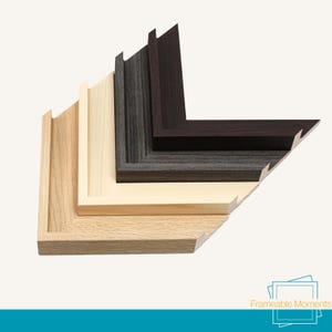 May include: A selection of wooden picture frame corners in shades of light oak, natural, grey, and dark brown. The frames are arranged in a layered, angled display, demonstrating their different profiles and finishes. The image is set against a neutral background.