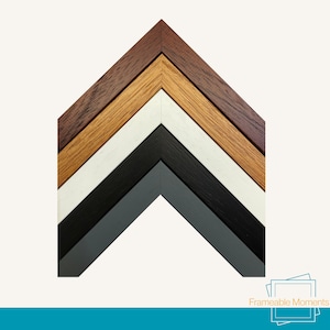 May include: A selection of wooden picture frame corners in shades of dark brown, light brown, white, black, and grey. The frames are arranged in a layered, angled pattern, displaying the different wood grains and finishes.