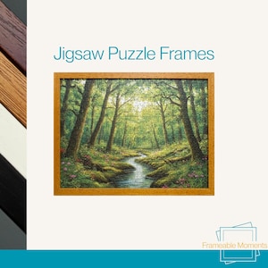 May include: A framed jigsaw puzzle depicting a forest scene with a stream, set within a light brown wooden frame. The image includes the text "Jigsaw Puzzle Frames" at the top.