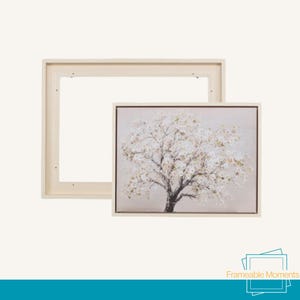 May include: A framed canvas print depicting a tree with white blossoms on a neutral backdrop. The print is in a light-coloured wooden frame, with a separate, matching frame. The image is labelled "Frameable Moments".