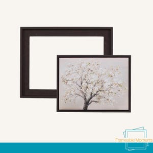 May include: A framed canvas print of a tree with white blossoms on a neutral background. The print is in a dark brown frame, with a separate empty frame of the same colour. The text "Frameable Moments" is in the bottom right corner.