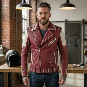 May include: A maroon leather motorcycle jacket featuring cream-colored side panels, silver-toned metal studs along the lapels and hem, a diagonal front zipper, multiple zippered pockets, a small flap pocket, and a belted waist with a silver buckle.