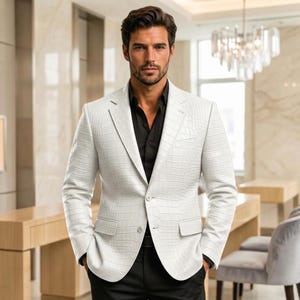 Puede incluir: Un blazer blanco con un patrón texturizado de piel de cocodrilo, con solapa de muesca, dos botones frontales y dos bolsillos con solapa, usado sobre una camisa negra lisa. El blazer tiene mangas largas y un corte estructurado y entallado.