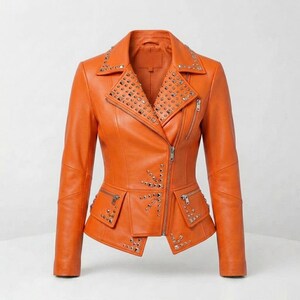 Puede incluir: Una chaqueta de color naranja brillante con cuello de muesca, mangas largas y cierre de cremallera asimétrico en la parte delantera. La prenda está adornada con tachuelas metálicas plateadas en las solapas, paneles frontales y dos bolsillos con cremallera en la cintura.