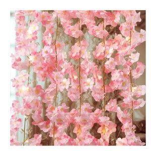 May include: A dense curtain of pink artificial cherry blossoms. The flowers are a soft pink with white centres, strung together on thin brown stems. Ideal for decorative purposes, the arrangement creates a full, floral display.