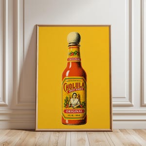 May include: A framed vertical poster featuring a centered illustration of a Cholula hot sauce bottle against a solid yellow background. The bottle has a round wooden cap, a red label with the text Original, and a yellow label with the text Cholula.