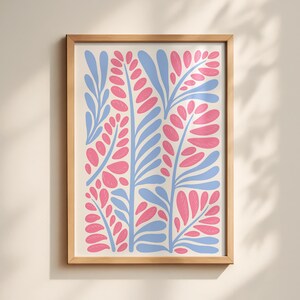 May include: A framed wall art print featuring a repeating botanical pattern of stylised light blue stems and vibrant pink leaves on a cream background. The artwork is enclosed in a simple, light-toned wooden frame with a clean, rectangular profile.