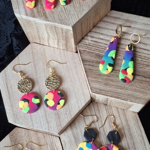 May include: Five pairs of drop earrings featuring colourful, multi-patterned shapes in neon pink, yellow, green and purple. The earrings include various geometric forms like arches, teardrops, circles and hexagons, accented with gold-tone metal hooks.