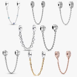 May include: A collection of eight silver and gold-toned safety chains for charm bracelets. Each piece features two circular end caps connected by a delicate metal chain, with variations including pavé stones, heart motifs, and engraved branding.
