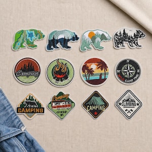 May include: A collection of twelve embroidered patches featuring outdoor themes including bears, mountains, campfires, palm trees, a compass, a camper van, a tent, and climbing gear. The designs use various colors like green, blue, orange, and black.