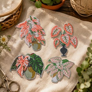 Puede incluir: Cuatro parches de tela bordados con diseños de plantas de interior en macetas. Cada parche muestra costuras detalladas de hojas en tonos rosa, verde y blanco, dispuestas en varios recipientes, incluyendo jarrones y macetas de formas distintas.