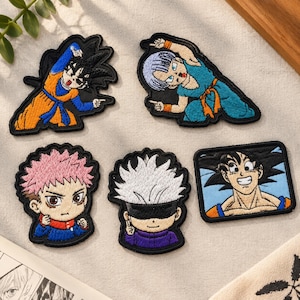 May include: Five embroidered fabric patches featuring anime characters. Two patches show characters in dynamic poses with orange and blue outfits. One patch depicts a character with pink hair, another with white hair and a black blindfold, and one rectangular patch shows a smiling character with black hair.