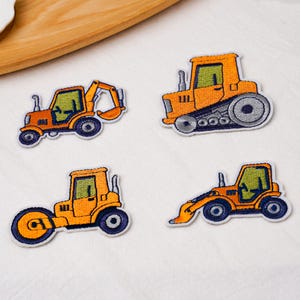 May include: Four embroidered patches featuring construction vehicles in bright orange, yellow, and dark blue. The set includes an excavator, a bulldozer with tracks, a road roller, and a backhoe loader, all with green-tinted windows and white borders.