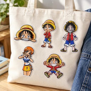 Pode incluir: Uma sacola de lona cor de creme com cinco patches bordados de personagens de anime. Os patches mostram quatro variações de um menino com chapéu de palha e camisa vermelha, e uma menina de cabelo laranja com uma blusa listrada azul e branca.