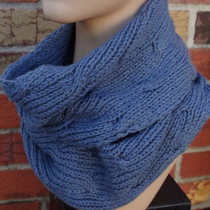 May include: A blue knitted neck warmer with a cable knit pattern.