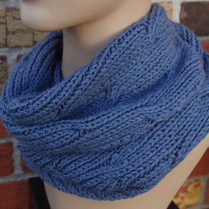 May include: A blue knitted infinity scarf with a cable knit pattern.