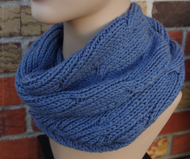 May include: A blue knitted infinity scarf with a cable knit pattern.