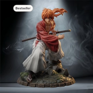 Può includere: Statuetta dettagliata di un personaggio anime, in posa con una katana. La figura indossa un abito rosso e bianco, con capelli arancioni. La base è un diorama dettagliato di un terreno roccioso. La parola "Bestseller" è in un ovale bianco.