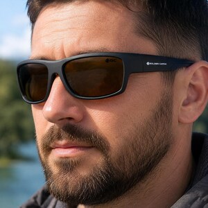 Peut inclure: Lunettes de soleil noir mat avec des montures rectangulaires et des verres marron foncé. La branche affiche le texte blanc Golden Catch, tandis que le coin supérieur du verre droit présente le petit logo noir GC avec une icône de poisson.