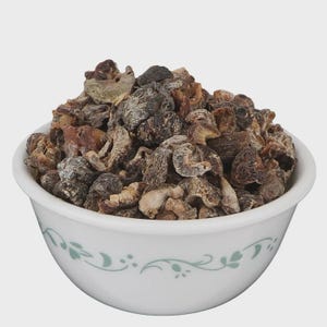 Puede incluir: Un cuenco de cerámica blanca con un delicado patrón de hojas de color verde claro alrededor del borde, lleno de un montón de trozos de fruta seca, de color marrón oscuro y arrugados. Las piezas tienen formas irregulares y texturas variadas.