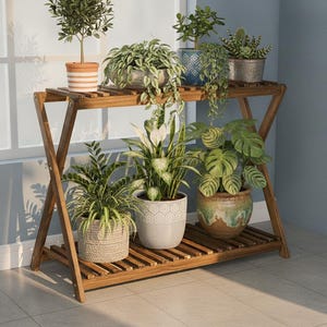 May include: A two-tier wooden plant stand with an X-shaped frame design. The stand features slatted shelves holding various potted plants, including a small tree, trailing vines, a peace lily, and a monstera, in assorted ceramic and metal pots.