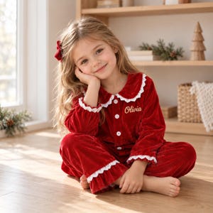 Può includere: Un set pigiama in velluto rosso a maniche lunghe composto da una parte superiore abbottonata con colletto e polsini rifiniti in pizzo bianco. Il nome Olivia è ricamato in filo dorato sul petto. I pantaloni abbinati hanno un orlo a balze.