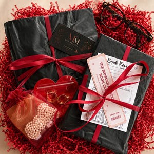 Peut inclure: Un coffret cadeau avec des paquets noirs attachés avec un ruban rouge, niché dans du papier rouge. Comprend une carte de visite, des lunettes, un sac en forme de cœur avec des boucles d'oreilles et un petit sac avec des perles.
